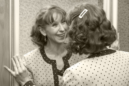 Attractive woman of average years cheerfully looks at the reflection in a mirrorの写真素材