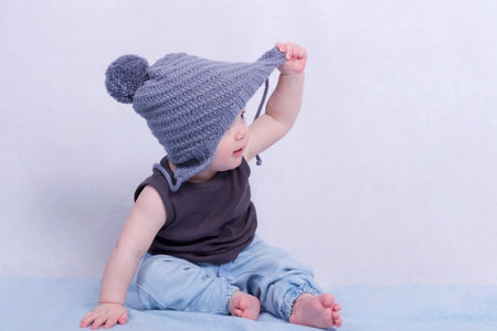 Cute infant boy in a grey hat and trying to take it off.