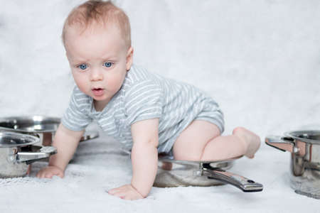 Mothers helper in a set of cooking pots and pans. Infant boy playing with a set of dishes. Cute toddler sitting on the frying panの写真素材