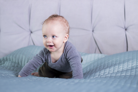 Wily faced baby boy sitting on the bed. Infant kid in playful mood. Happy toddler playing indoorの写真素材