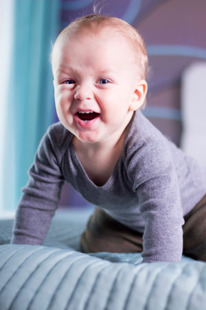 Laughing infant boy looking at camera. Open mouthed smiling toddler kid.