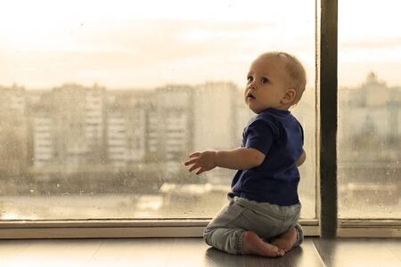 Cute baby boy looking through the window to the big city.の写真素材
