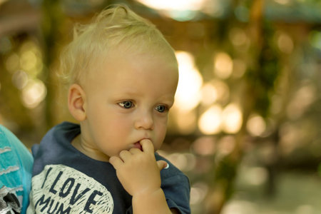 Cute blue-eyed thoughtful toddler. Blurred background. Meditative toddler in t-short with sign i love mumの写真素材