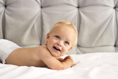 Funny smiling toddler lying on the bed against the grey background. Copy spaceの写真素材