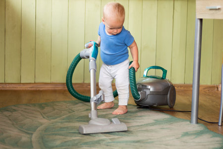 Cute toddler cleaning up the kitchen with vacuum cleanerの写真素材