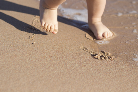Legs of children stand on the beach. Baby feet in the sand. Summer beach background. Summertime holidays concept. Copy space.の写真素材
