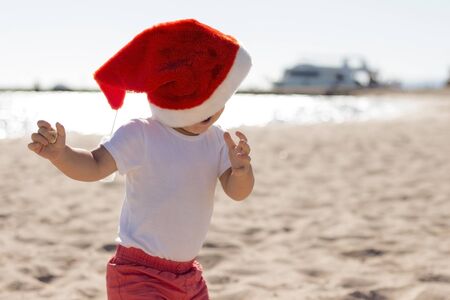 Funny little boy in Santa Christmas red hat having fun in the ocean bankの写真素材