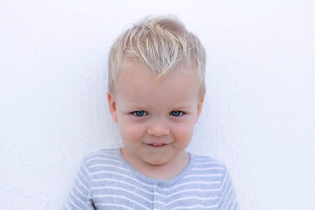 Emotions. Shy toddler against wall. Close-up portrait of cute little boyの写真素材