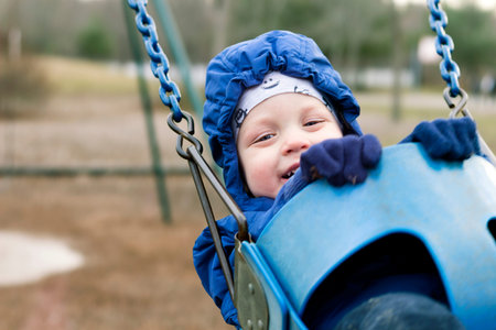 Happy smiling toddler on a swing on the playground. Spring or autumn shotの写真素材