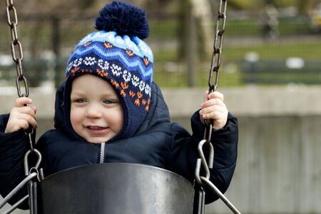 Happy smiling toddler on a swing on the playground. Spring or autumn shotの写真素材