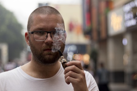 White caucasian handsome bearded man and stylish glasses smoking pipe on the street. Close up portrait.の写真素材