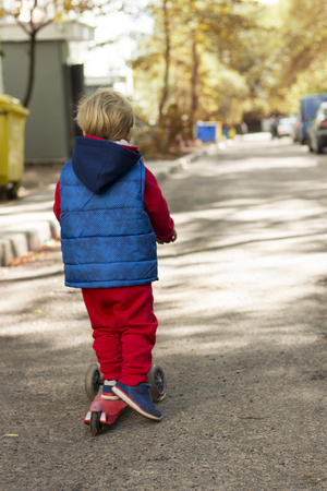 Little child learning to ride a scooter in a city park on sunny day. Cute preschooler boy without safety helmet riding a roller. Kids play outdoors. Active leisure and outdoor sport for children.の写真素材