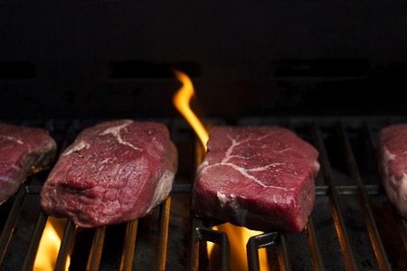 raw beef steak cooking over flaming grillの写真素材