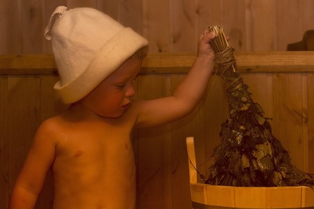 Beauty, healthcare. baby Boy relaxing in the sauna Toddler with broom and hat in russian sauna or bathの写真素材
