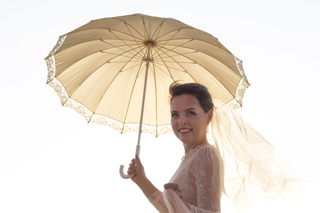 Portrait of a smiling beautiful woman holding umbrella and looking at camera light backgroundの写真素材