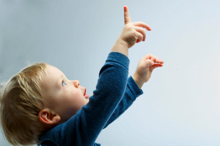 Beautiful blonde toddler looking up. Boy showing, kid holding his hand up. Copy space