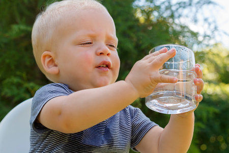 portrait of cute baby boy with glass of waterin his handsの写真素材