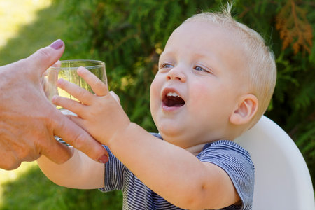 Portrait of a baby boy drinking a glass of water. Outdoor shot