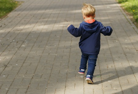 Back view of baby boy running and jumping in the spring or autumn alley.の写真素材