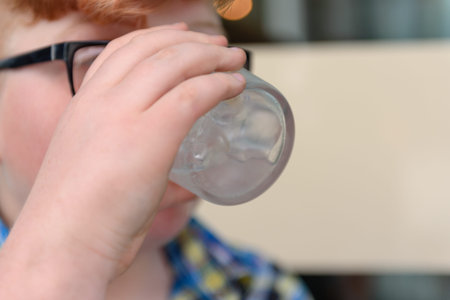 Cute red-haired boy with glasses in an urban context drinks ice water with lemon and ice. The boy...