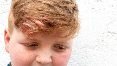 Plump red-haired boy is smiling. A boy in a plaid shirt stands on a wall background and smiles.