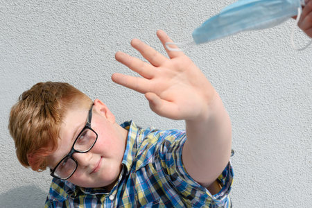 The red-haired boy with glasses refuses to receive the surgical mask offered by an adult. Boy with glasses and plaid shirt who refuses to wear a surgical mask.の写真素材