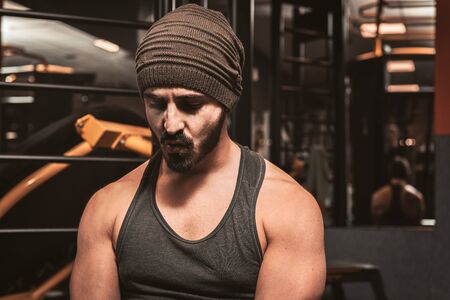 Muscular tired bodybuilder guy showing his muscular body taking a break from running or exercise sitting in the gym. Fitness young sporty man resting in workout. Train in a healthy way.の写真素材