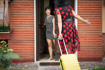 Woman welcomes her friend in vacation home. Guest wears dress for special events with decorations.の写真素材