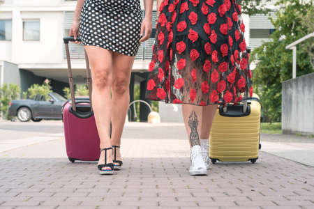 Cropped photo from below of two elegant tourist women walking with suitcases on the flowery street of the city.の写真素材