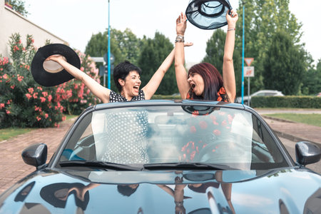 Two elegant women driving a convertible car enjoying vacation having fun on the road.