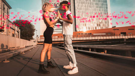 Couple of young man and woman with different ethnic origin in the city with red hearts flying against the background of a skyscraper.の写真素材