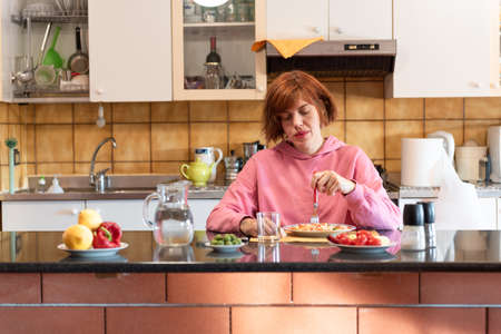 Young pretty woman eats alone in her kitchen.の写真素材