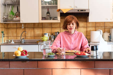 Young pretty woman eats in her kitchen and drinks water from the glass.の写真素材