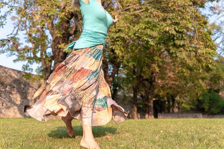 Beautiful barefoot girl in a long colorful skirt is dancing in natural backgroundの写真素材