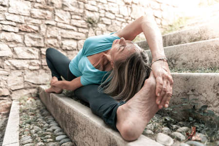 Adult woman does sports exercise. Yoga teacher doing an asana on the old city staircase.の写真素材