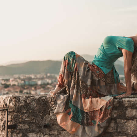 Adult woman does sports exercise. Yoga teacher doing an asana on the old city wall.の写真素材