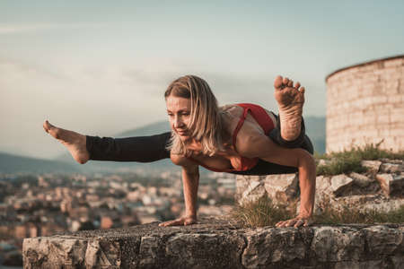 Adult woman does sports exercise. Yoga teacher doing an asana on the old city wall.の写真素材