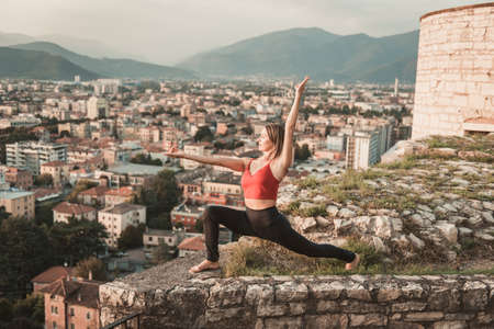 Adult woman does sports exercise. Yoga teacher doing an asana on the old city wall.の写真素材