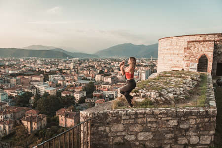 Adult woman does sports exercise. Yoga teacher doing an asana on the old city wall.の写真素材