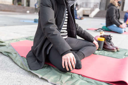 Yoga teachers protesting against the blockade and restrictions of Covid-19 in a square in Brescia, Italy. Shot of the hands resting on the knees of the crossed legs. People are meditating.の写真素材
