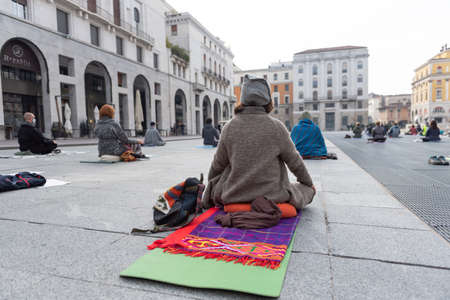 Yoga teachers protesting against the blockade and restrictions of Covid-19 in a square in Brescia, Italy. The people sitting on the fitnes mat and are meditating. Shooting from the back.の写真素材