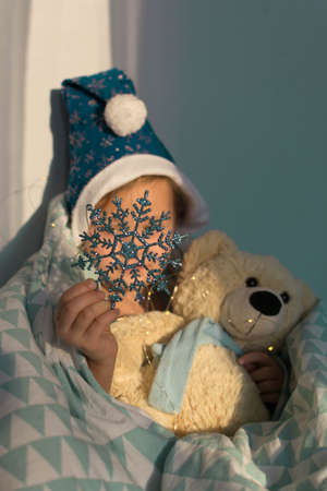 Little girl in santa hat sleeping in bed with teddy bear and snowflakeの写真素材