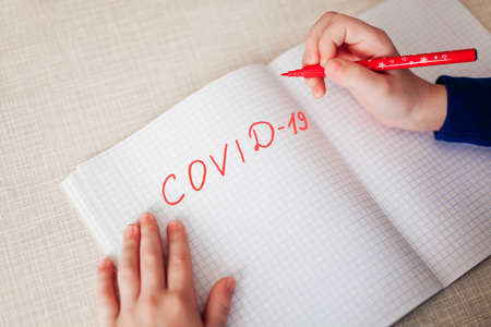 Distance learning online education. The inscription Covid 19 with a red pen in a notebook, which lies on a wooden table. Place for text. View from above.の写真素材