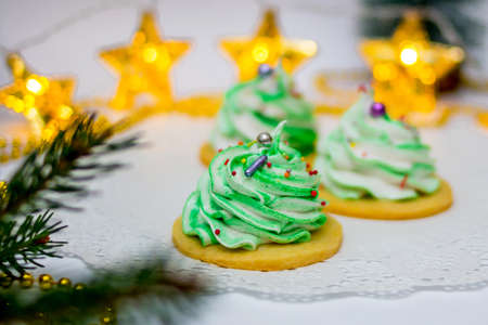 Three green herringbone-shaped marshmallows on a white openwork napkin. The background consists of a garland in the form of glowing stars. Concept of holiday - Christmas, New Yearの写真素材