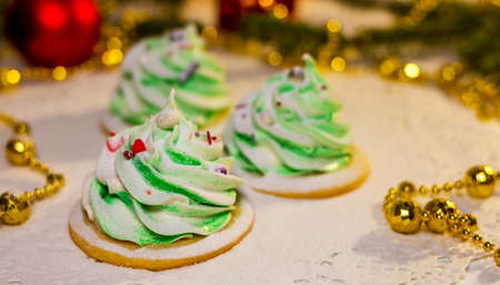 Three green marshmallows in the shape of a Christmas tree on a white delicate napkin. Background consists of golden garland, Christmas tree and red balls. Concept of the holiday - Christmas, New Year.の写真素材