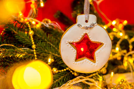 Christmas white gingerbread in the form of a Christmas tree ball with a star in the middle. Red background with a Christmas tree and golden garlands. Concept of holiday - new year, Christmas. Bannerの写真素材