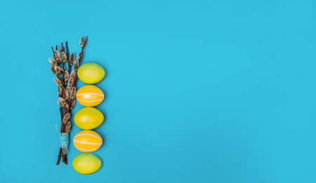 Five multi-colored Easter eggs lie near the branches of a willow on a blue background. View from above. Place for text. Banner. Easter card. Easter background. Easterの写真素材