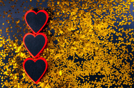 Three red hearts lie on a black background with gold sequins. The concept of the holiday is Valentine's Day, February 14, Mother's Day. Place for your text. A greeting card. Bannerの写真素材
