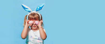 A little girl with white hair and bunny ears on her head on a blue background and closes her eyes...