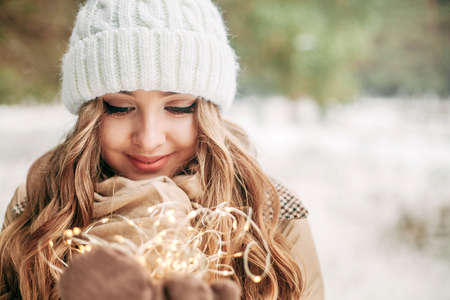 Beautiful girl with a Christmas garland in her hands. Portrait of a girl close-up in the winter forest. Concept - new year, Christmas, greeting card, banner. A place for textの写真素材
